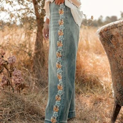 Calças de ganga azul claro com bordado floral lateral e camisa branca num campo seco.