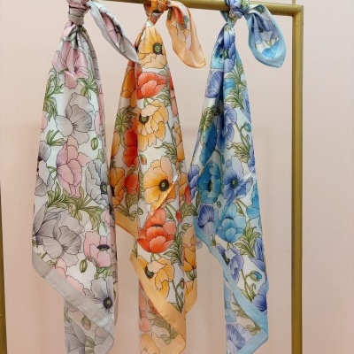 Três lenços florais pendurados numa haste dourada com padrões em rosa, laranja e azul