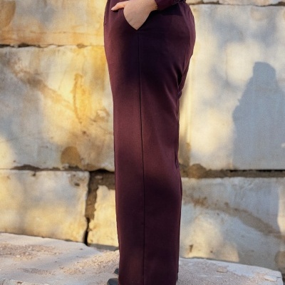 Calças cor vinho com bolso e blusa de renda na mesma cor, cenário exterior com pedra.