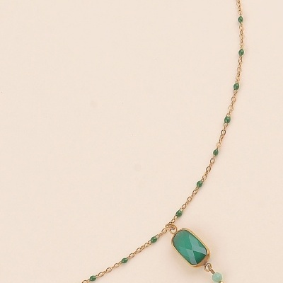 Colar dourado com contas verdes e pendente retangular verde em fundo bege