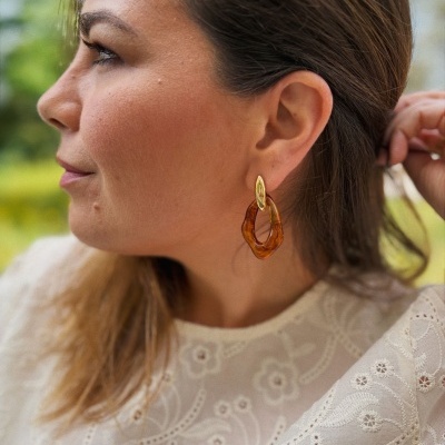 Mulher de perfil a usar brinco dourado e castanho com blusa branca bordada.