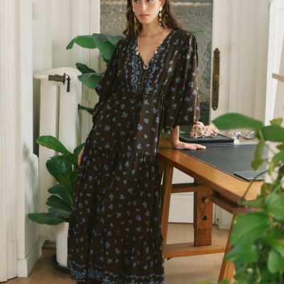 Vestido longo castanho com flores azuis em ambiente interior com planta e mesa de madeira