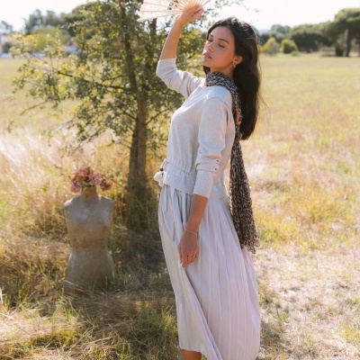Mulher em campo com vestido e camisola claras, abanador e lenço animal print.