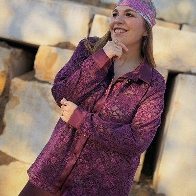 Mulher com lenço cor-de-rosa e camisa roxa com renda em fundo de pedras