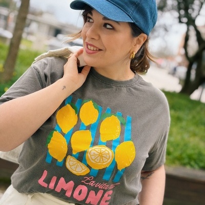 Pessoa com t-shirt cinza estampada com limões e texto La vita di LIMONE e boné azul com texto branco.