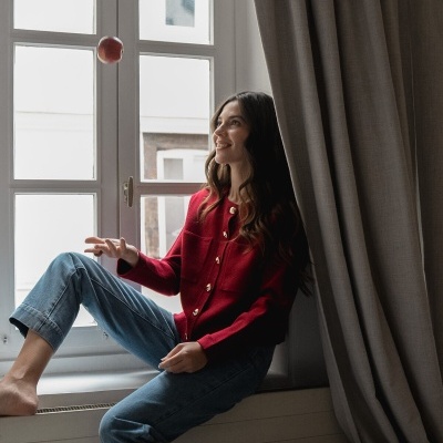 Mulher sentada na janela a lançar uma maçã para o ar.