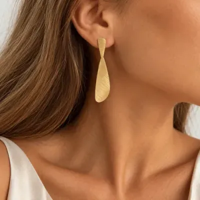 Brinco pendente dourado com textura escovada em orelha de mulher
