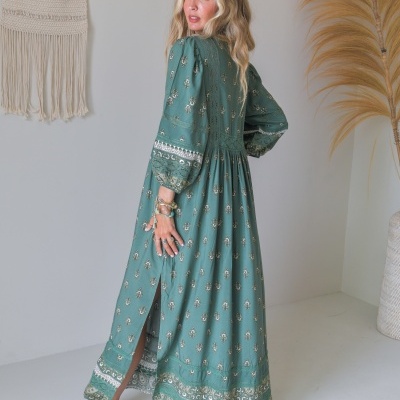 Vestido longo verde com padrão floral e renda, usado em interior minimalista.