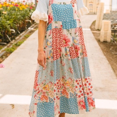 Vestido comprido patchwork floral e bolinhas azul, vermelho e rosa, usado numa estufa com flores.
