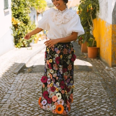Mulher com saia longa floral e blusa branca em rua com calçada portuguesa