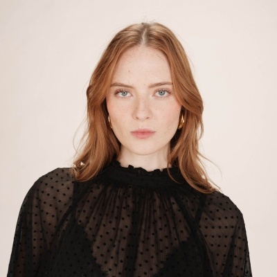 Mulher com blusa preta transparente de bolinhas e brincos dourados