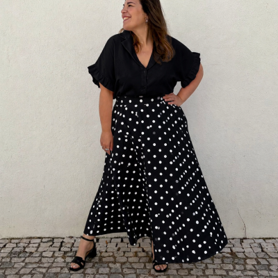 Mulher com camisa preta e saia preta com bolinhas brancas numa calçada