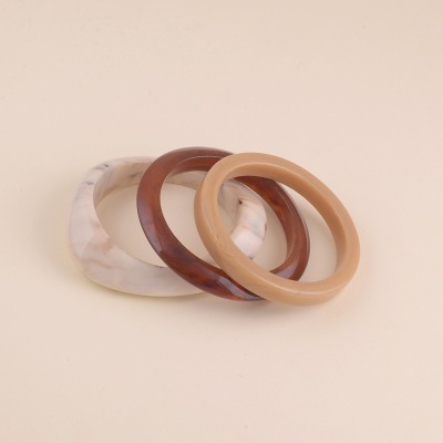 Conjunto de três pulseiras redondas em tons de bege e castanho sobre fundo bege.