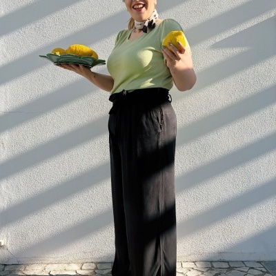 Mulher com roupa casual a segurar frutas amarelas em parede branca com sombras