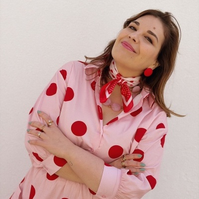 Mulher com vestido rosa de bolinhas vermelhas e acessórios vermelhos em fundo branco