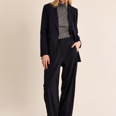 Mulher com blazer e calças pretas largas, camisola cinza e botins castanhos.