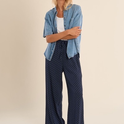 Mulher com camisa de ganga azul clara, t-shirt branca, calças largas azuis com pontos brancos e sapatilhas claras