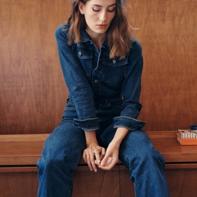 Mulher com macacão de ganga azul escuro sentada num banco de madeira