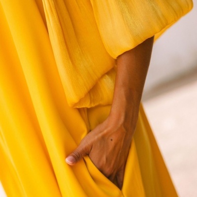 Vestido amarelo com bolso e textura plissada visível próximo à mão de uma pessoa