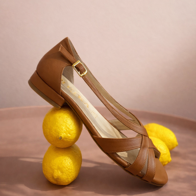 Sapato feminino castanho de couro sobre limões amarelos.