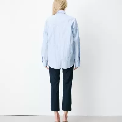 Pessoa de costas com camisa azul clara de riscas e calças pretas