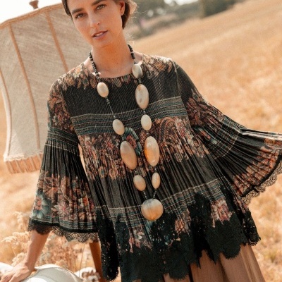 Blusa feminina floral com mangas amplas e colar grande em ambiente de campo