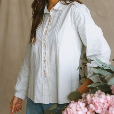 Blusa branca bordada com botões e calças de ganga azuis junto a flores cor-de-rosa