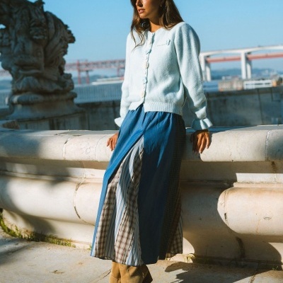 Mulher com cardigan branco e saia azul com padrões verticais em ambiente exterior