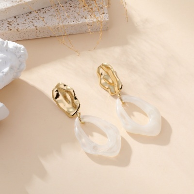 Brincos dourados com pendente branco em resina sobre superfície bege