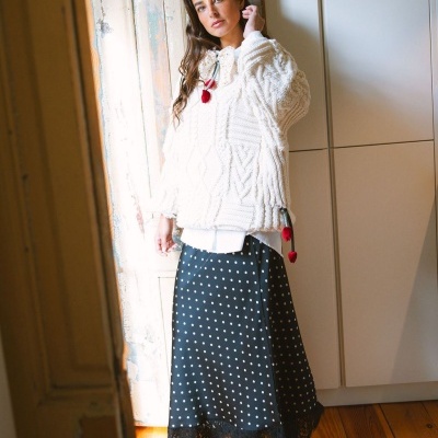 Mulher com camisola de malha branca e saia preta de bolinhas com renda