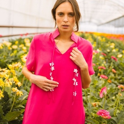 Vestido rosa vibrante com detalhes de flores brancas em mulher na estufa de flores