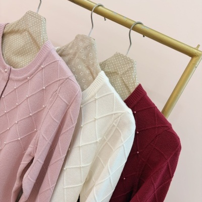 Três cardigans de malha rosa claro, branco e vermelho pendurados em cabides revestidos de tecido bege estampado com estrelas.