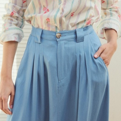 Calças azuis claras com pregas e bolso, combinadas com camisa creme com riscas e flores bordadas
