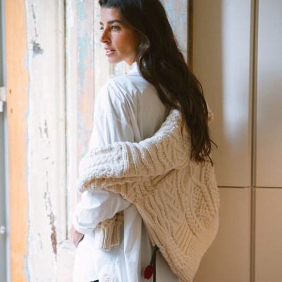 Mulher com camisa branca e camisola creme de malha com padrão trançado