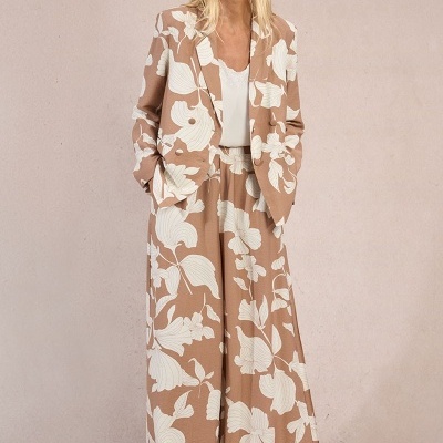 Conjunto feminino bege com padrão de folhas brancas, blusa branca e sandálias castanhas num fundo bege.