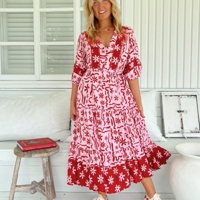 Vestido midi rosa com padrão floral vermelho usado por mulher com ténis brancos.