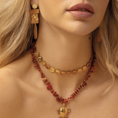 Colar duplo com contas vermelhas, pendente dourado e colar dourado texturizado em pescoço de mulher.