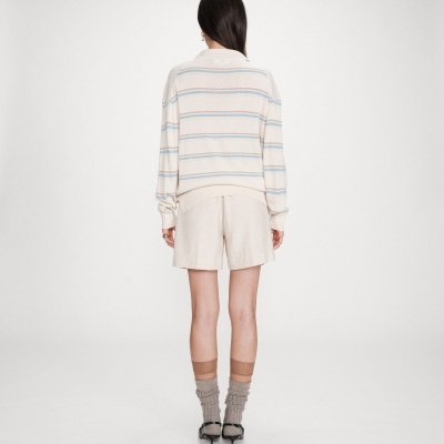 Mulher de costas com camisola riscada creme, calções creme, meias bege e sapatos pretos