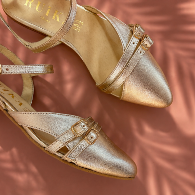Sapatos de senhora dourados em couro com fechos de fivela sobre fundo rosa