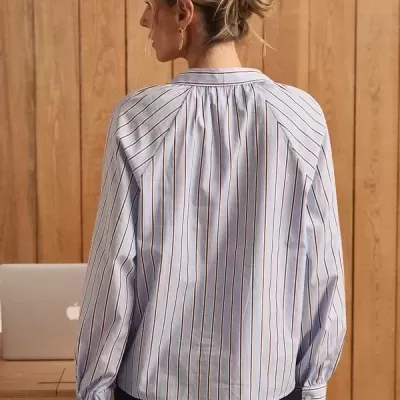 Blusa de manga comprida às riscas vista de costas, mulher de cabelo apanhado, parede de madeira ao fundo