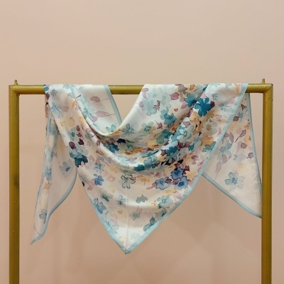 Lenço sedoso floral em tons azuis e bege pendurado num suporte amarelo.