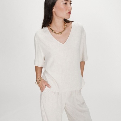 Mulher com conjunto de roupa branco de tecido leve e textura ligeiramente rústica com colar e pulseiras douradas