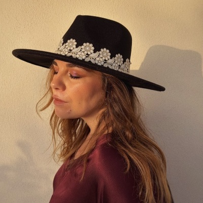 Mulher de perfil com chapéu preto de aba larga e flores brancas bordadas