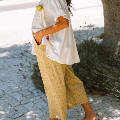 Calças amarelas com padrão floral e blusa branca com detalhe floral usada por mulher ao ar livre
