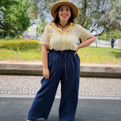 Mulher de chapéu castanho com blusa bege e calças largas azuis ao ar livre