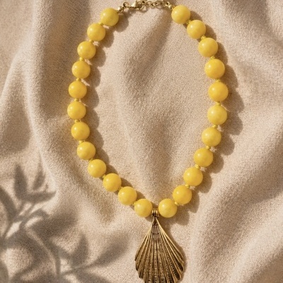 Colar amarelo com pendente dourado em forma de concha sobre tecido bege