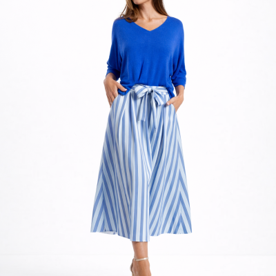 Mulher com camisola azul e saia riscada azul e branca com laço