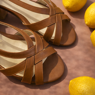 Sandálias castanhas de couro com tiras cruzadas e limões amarelos ao redor