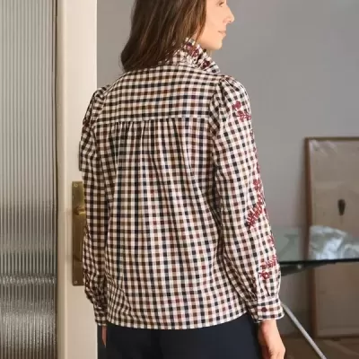 Blusa xadrez com bordados vermelhos e gola alta usada por mulher vista de costas.