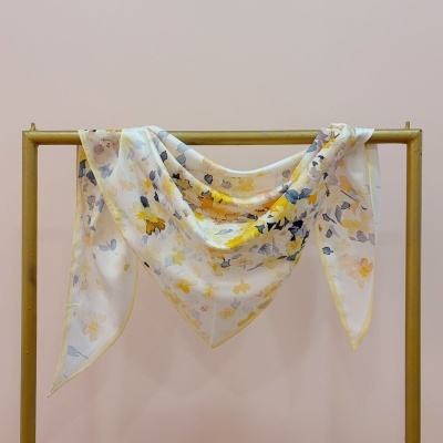 Lenço branco com padrão floral amarelo e azul pendurado num cabide dourado